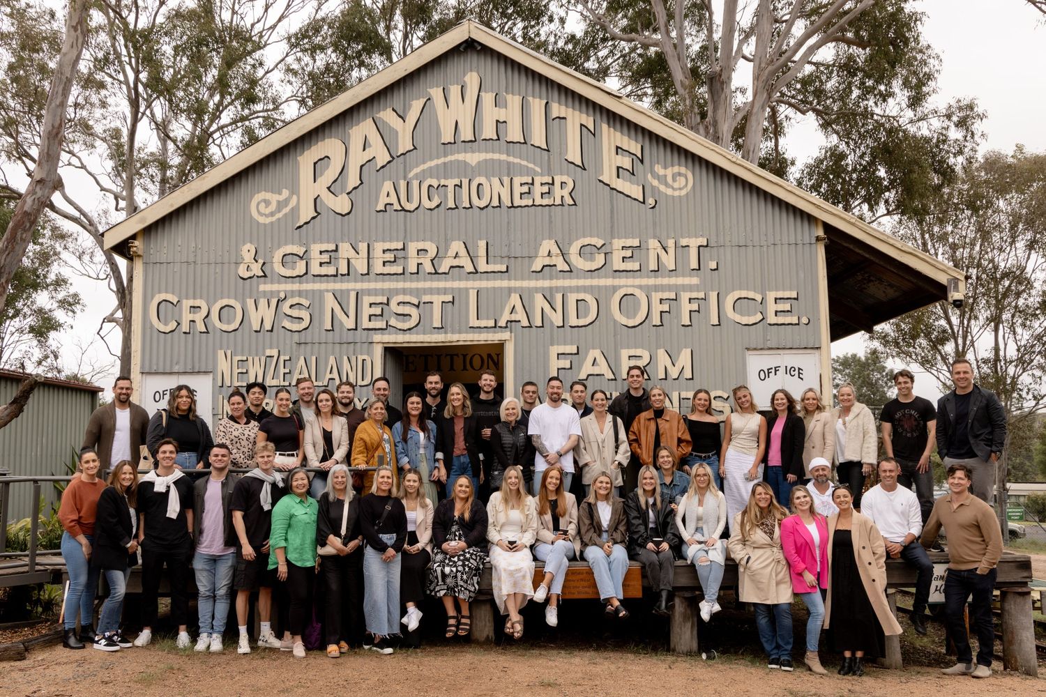 Large group posed in front of rustic Ray White Auctioneer building with vintage signage. Crows Nest Queensland.