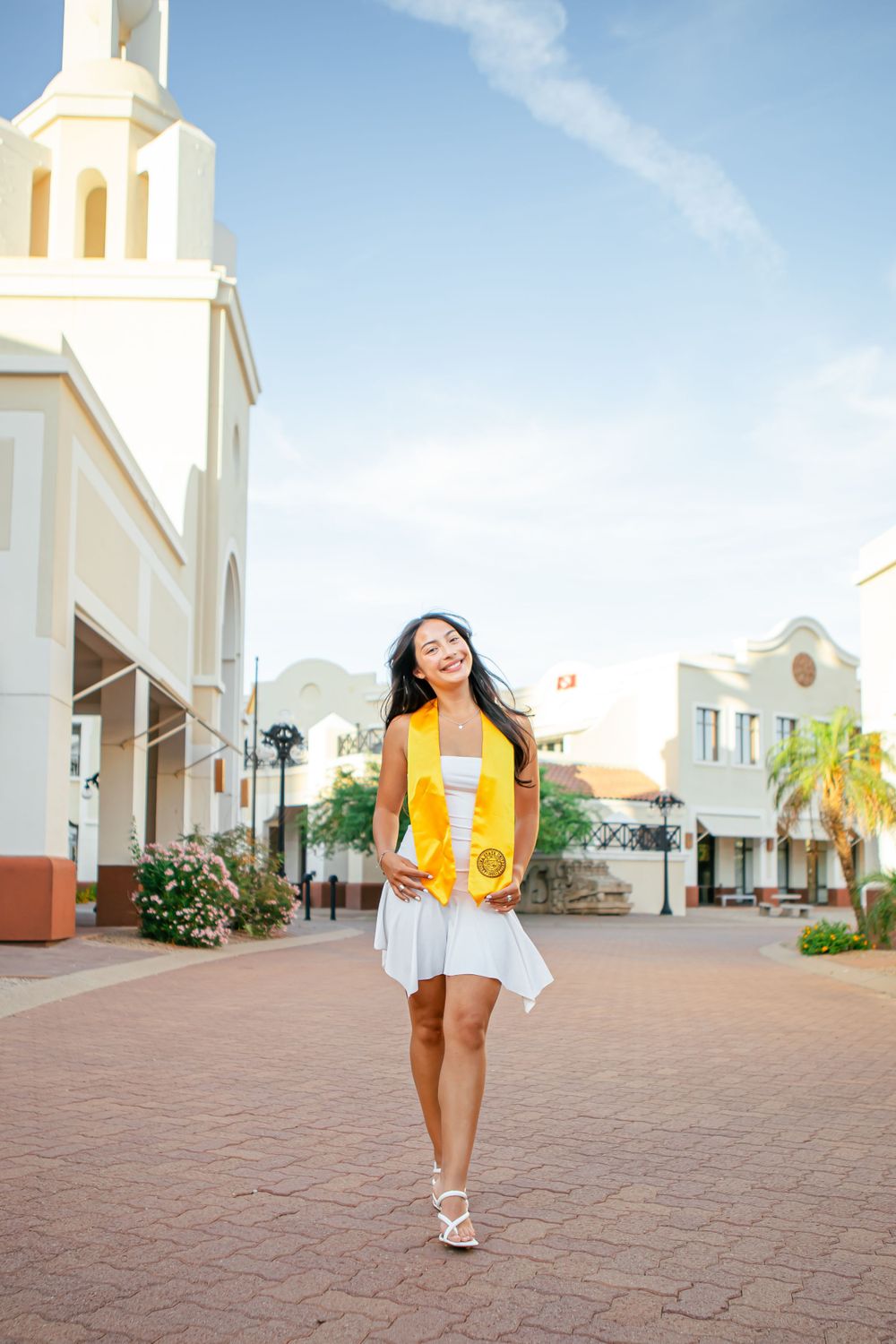 Person in yellow and white outfit walking across brick courtyard with white Spanish colonial architecture.