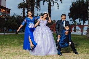 Family posing playfully on grass with palm trees in background, wearing formal attire.