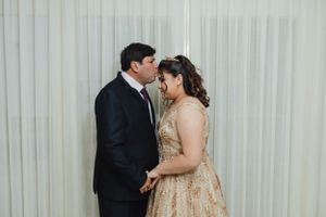 Couple in formal attire sharing an intimate moment against a white curtain backdrop at a celebration.