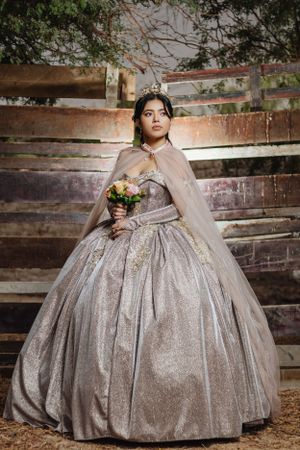 Young woman in a sparkly silver ballgown poses in front of rustic wooden backdrop.