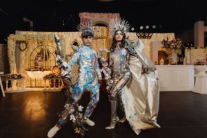Two people in elaborate metallic costumes dancing at a themed celebration with ornate decorations.