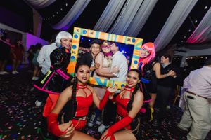 Party guests posing with colorful photo frame props at a festive celebration with confetti.
