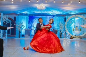 A couple dances in an elegant ballroom decorated with blue lighting and fabric draping for a quinceañera celebration.