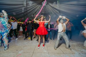 Guests dance and celebrate at a party with colorful lighting and white fabric ceiling decorations.