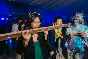 Guests attempt the limbo dance under a pole at a festive party with blue lighting effects.