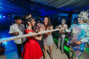 Partygoers play limbo under a pole while a person in a sparkly costume watches.