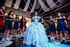 A celebrant in a blue ballgown poses with bridesmaids under sparkling lights at a quinceañera celebration.