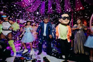 Party guests dancing under purple lighting with confetti falling during a festive celebration.