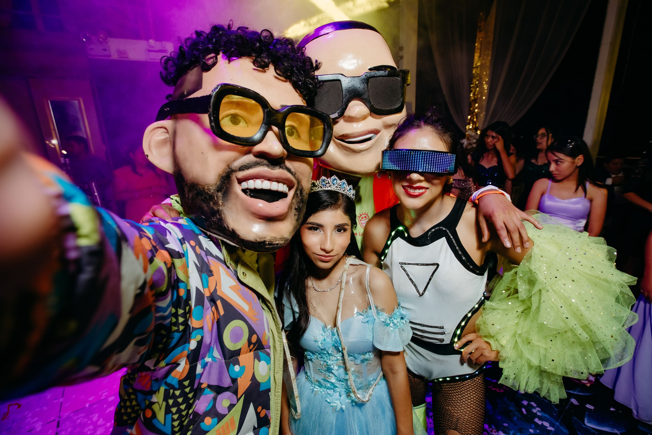 Group of party guests wearing sunglasses pose together under vibrant purple lighting.