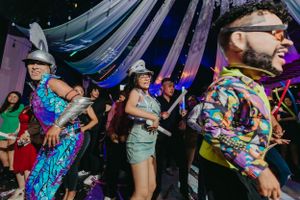 Party guests dance and celebrate under draped purple lighting at a festive event.