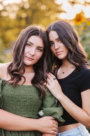 Two young women in casual attire pose together outdoors during golden hour sunset.