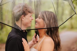 Couple embracing and laughing together under a transparent umbrella in a forest.