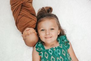 Two young children laying on white background with one wearing a green patterned dress.