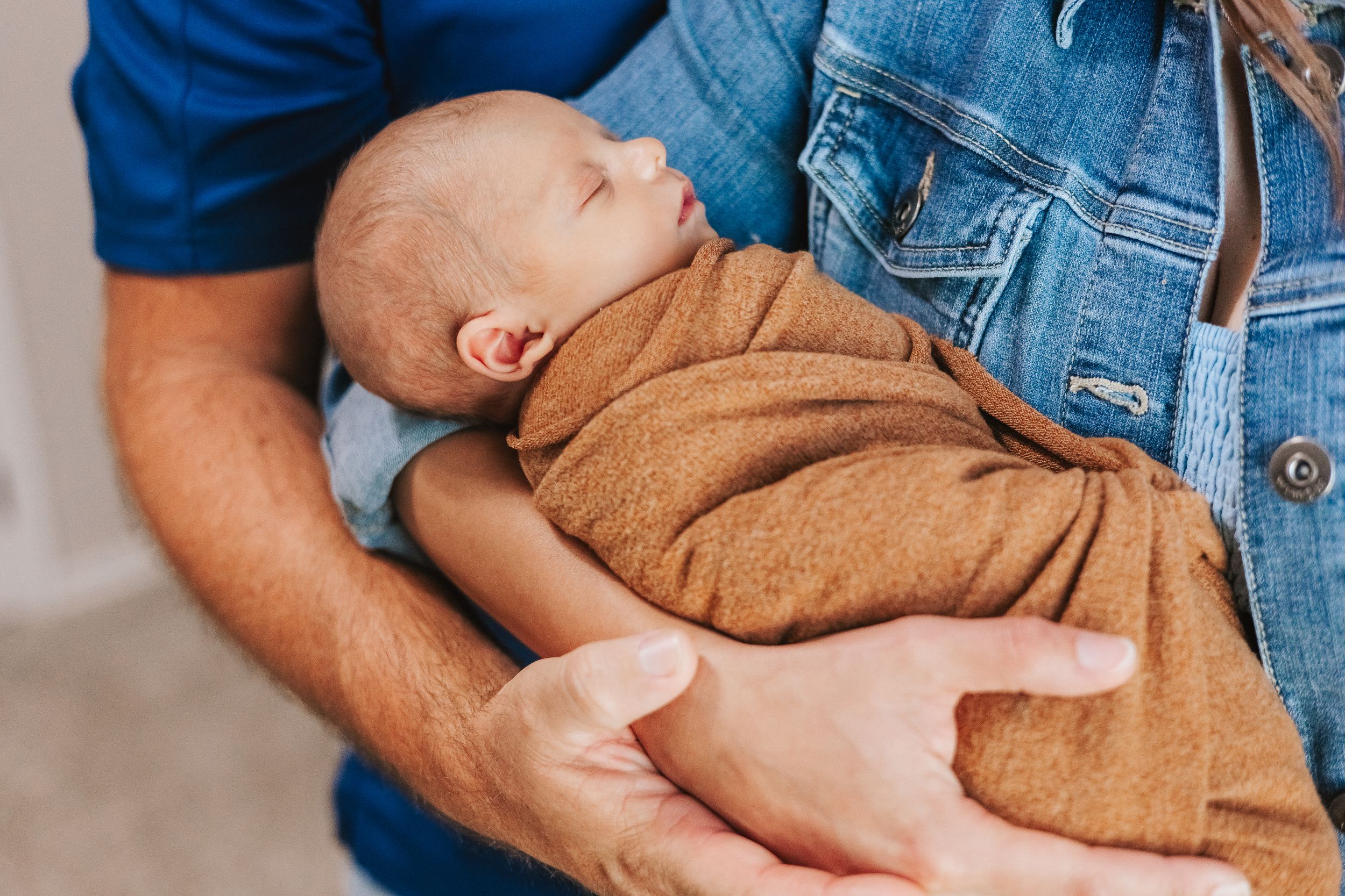 A sleeping infant wearing brown clothing being cradled in someone's arms.