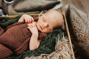 Sleeping baby in brown knit sweater nestled in green and beige textiles.