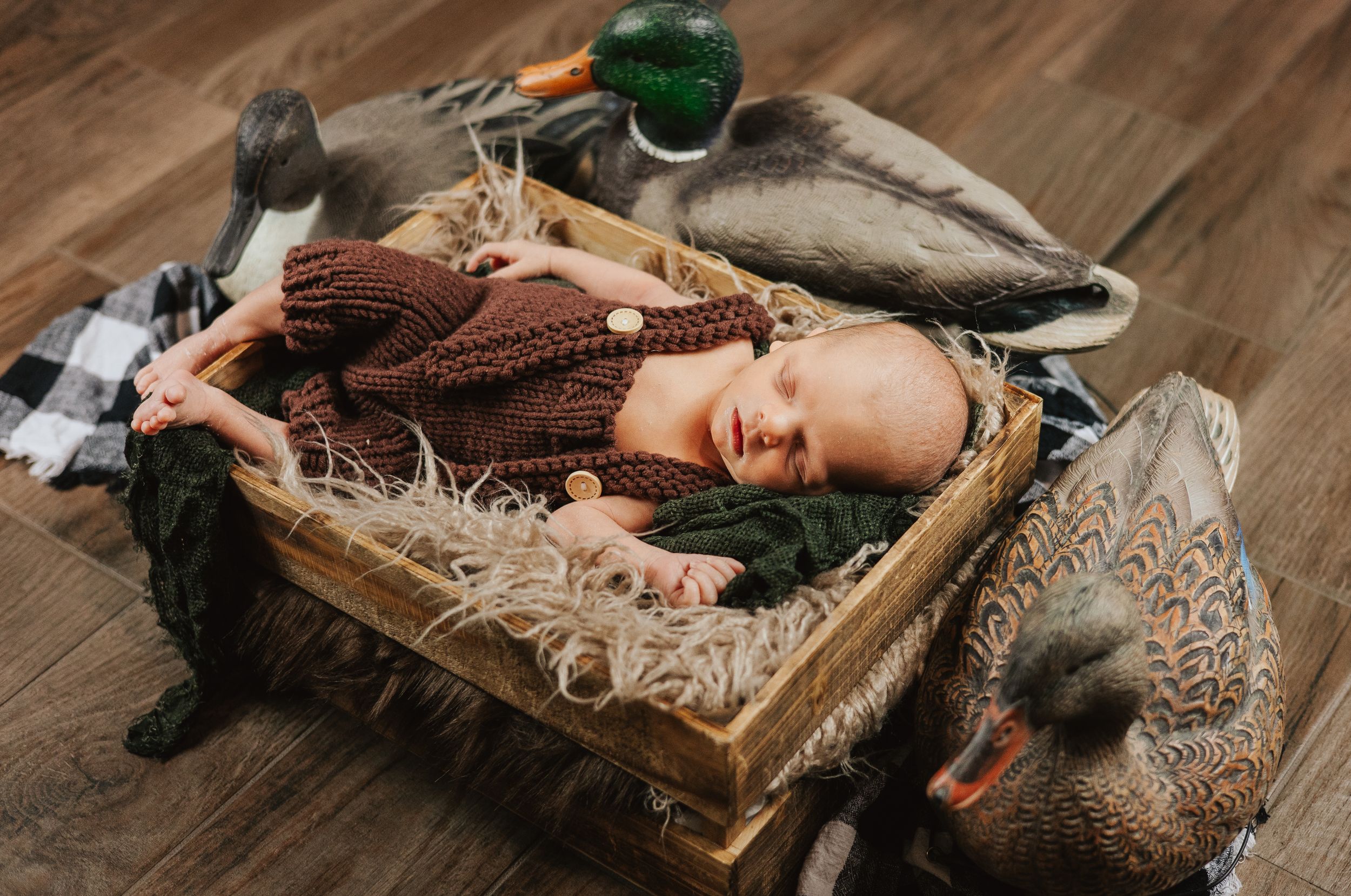 Sleeping newborn in brown knit outfit surrounded by vintage decor on wooden floor.