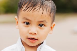 Baby in white outfit smiling at camera against neutral background.