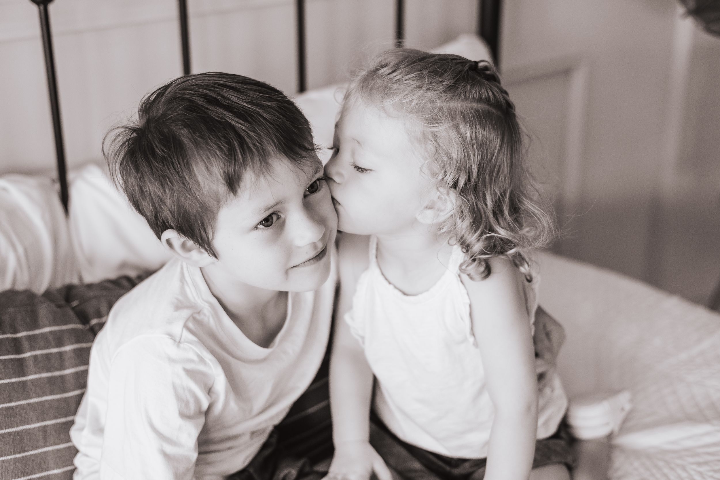 Children play and laugh together on bed during indoor family photo session.