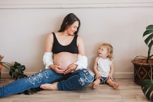 Tender moments captured between parent and child against neutral wall with indoor plants.