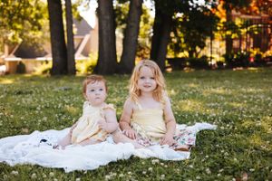 Children sitting on blanket in sunlit grass during golden hour.