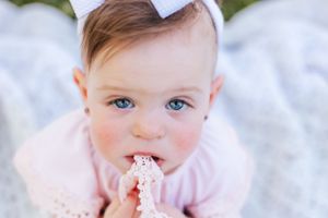 Baby in pink outfit with white bow accessory against soft background.