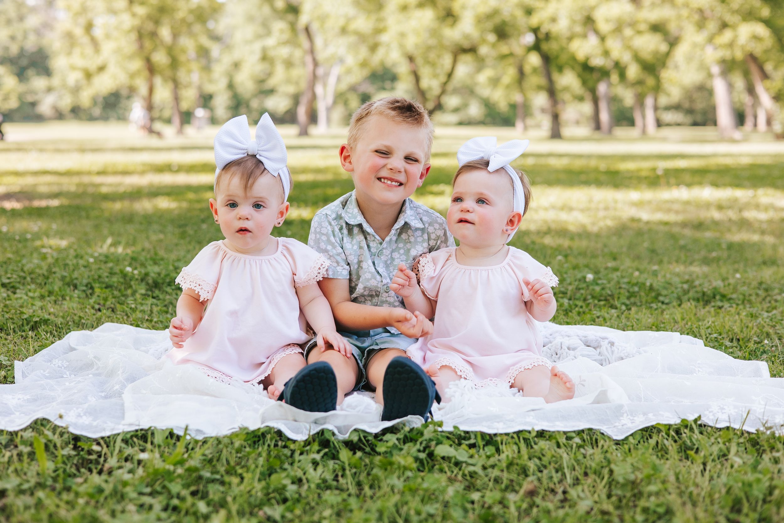 Family sitting together on white blanket in sunny park setting.