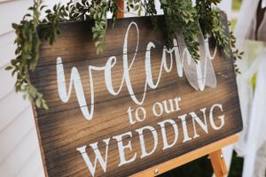 Rustic wooden wedding welcome sign decorated with greenery and white calligraphy.