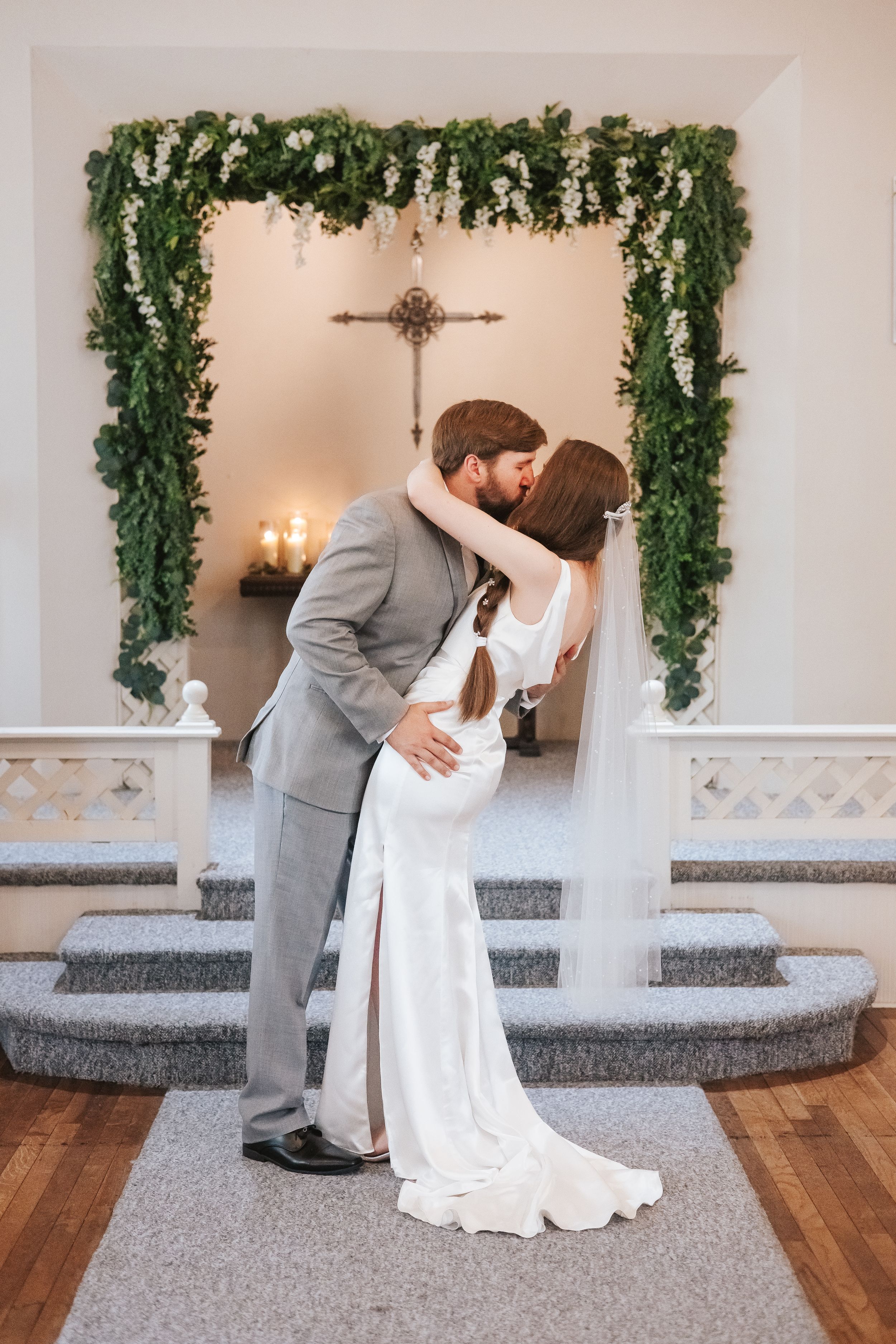 Wedding couple shares romantic dance moves in elegant white venue with greenery decor.