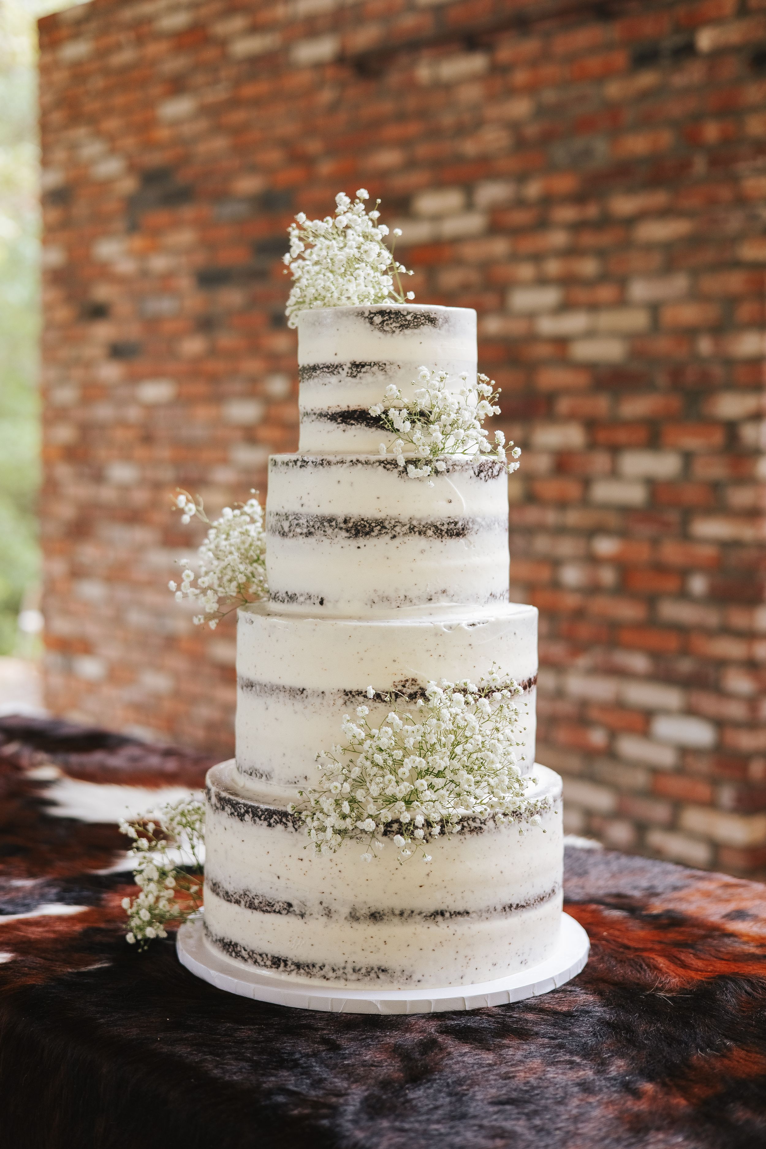 Three-tiered white wedding cake decorated with baby's breath flowers against brick wall background.