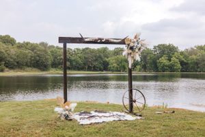Rustic wooden arch setup overlooking a serene lake surrounded by trees for an outdoor wedding ceremony.