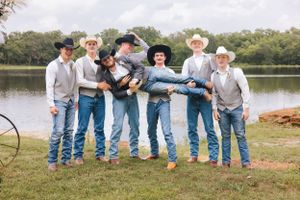 Wedding party in blue jeans and cowboy hats sitting casually by a lakeside.