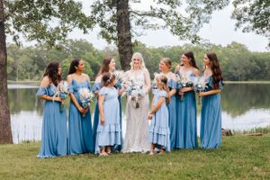 Bridesmaids wearing light blue dresses gathered together by a lake for wedding photos.