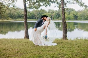 Wedding couple poses under trees by a scenic lake during their countryside celebration.
