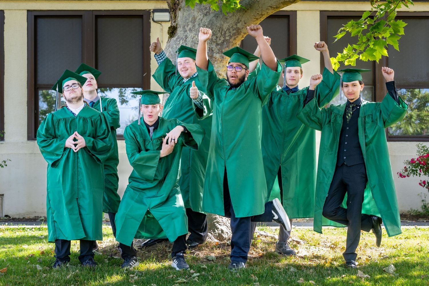 Graduates in green robes jumping for celebratory photo on sunny day.