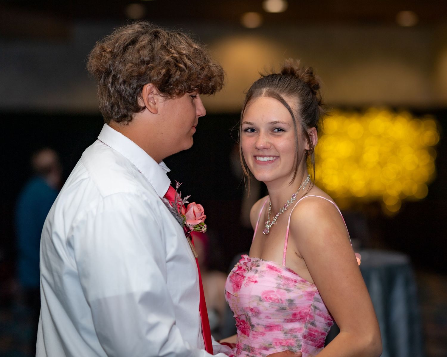 A couple dances together at an indoor reception venue with warm lighting in the background.