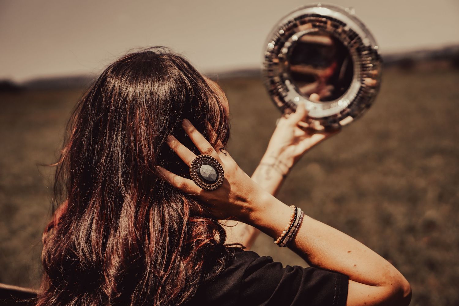 Back view of someone holding up a circular mirror outdoors during golden hour.