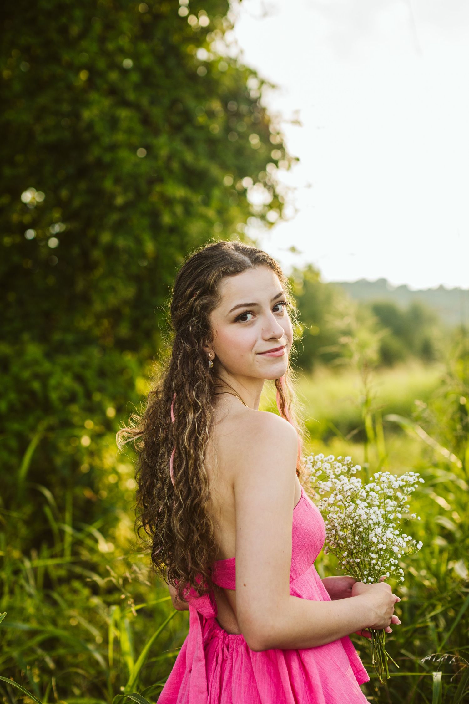 Female student in pink dress holding flowers for a senior session