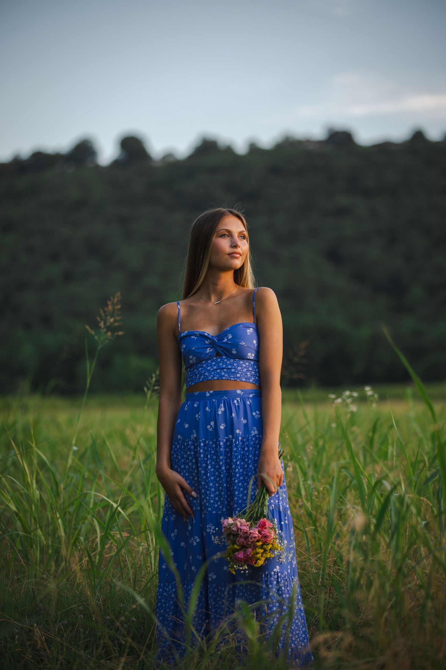 female student in purple summer dress holding flowers standing in a field