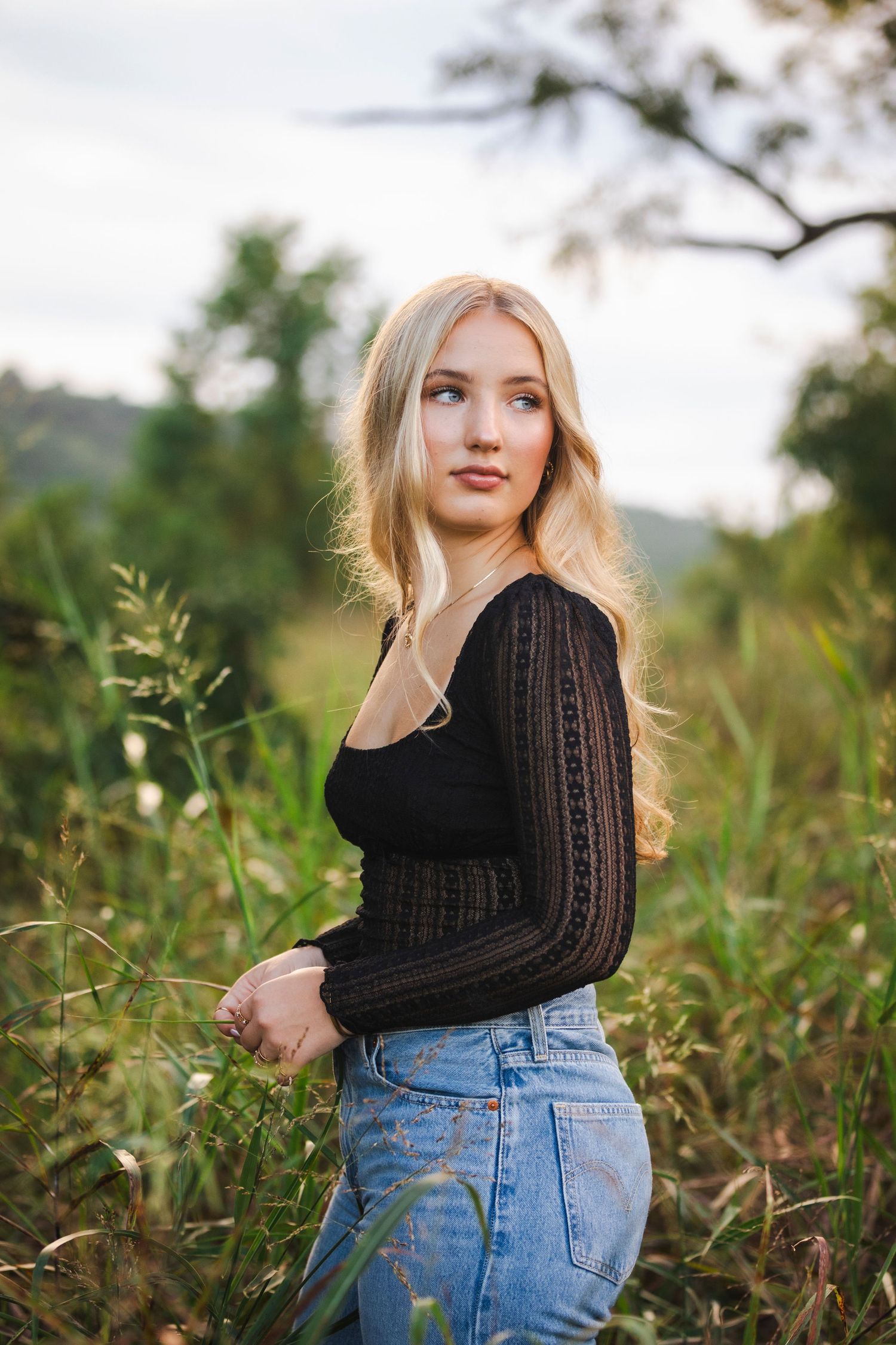 female in jeans and black shirt with blonde hair standing in tall grass