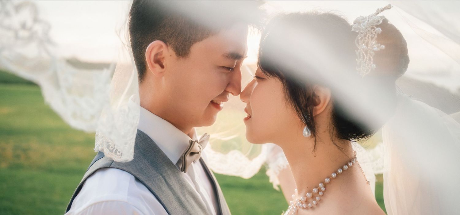 Close-up romantic portrait of a bride and groom looking into each other's eyes under a sheer bridal veil.