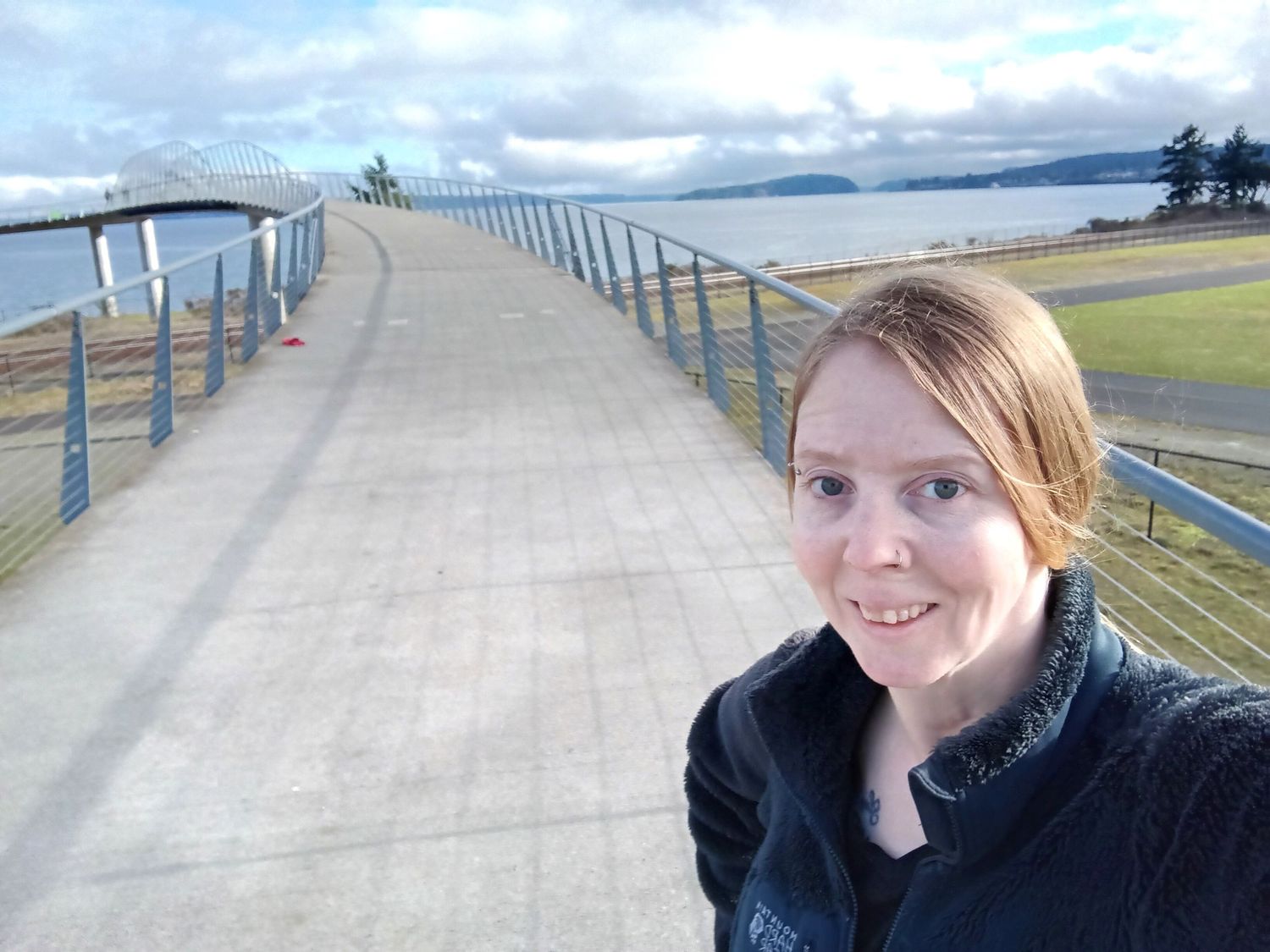Walkway along waterfront with cloudy sky and mountains in background.