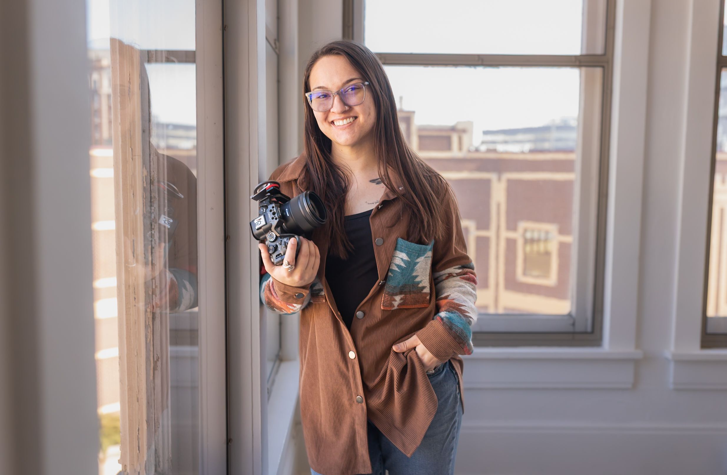 A casual portrait of a photographer sitting cross-legged outdoors with camera equipment.