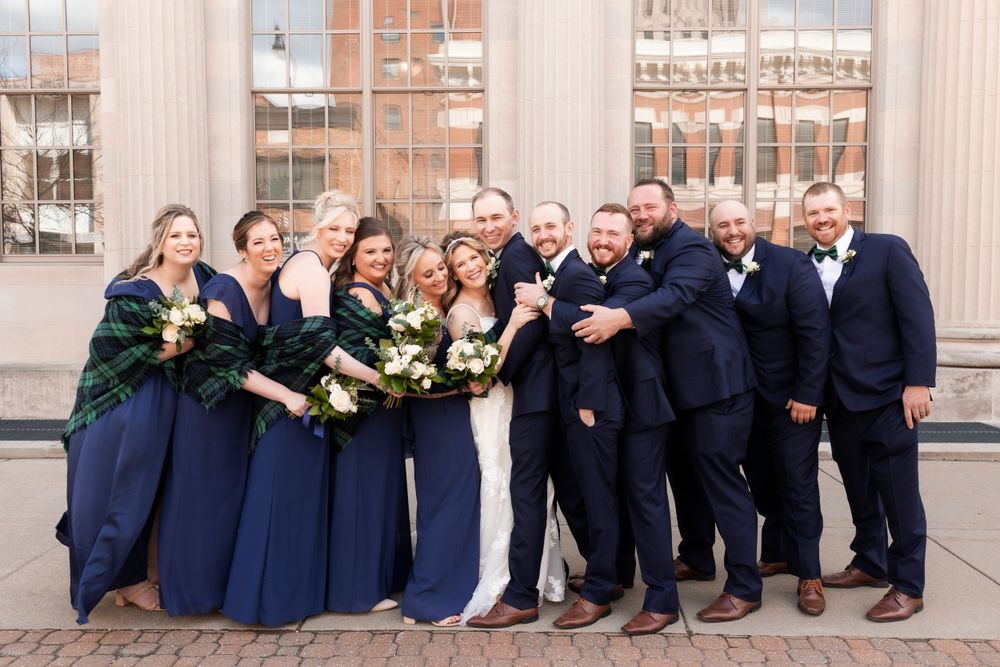 Large wedding party in navy attire smiling together outdoors.