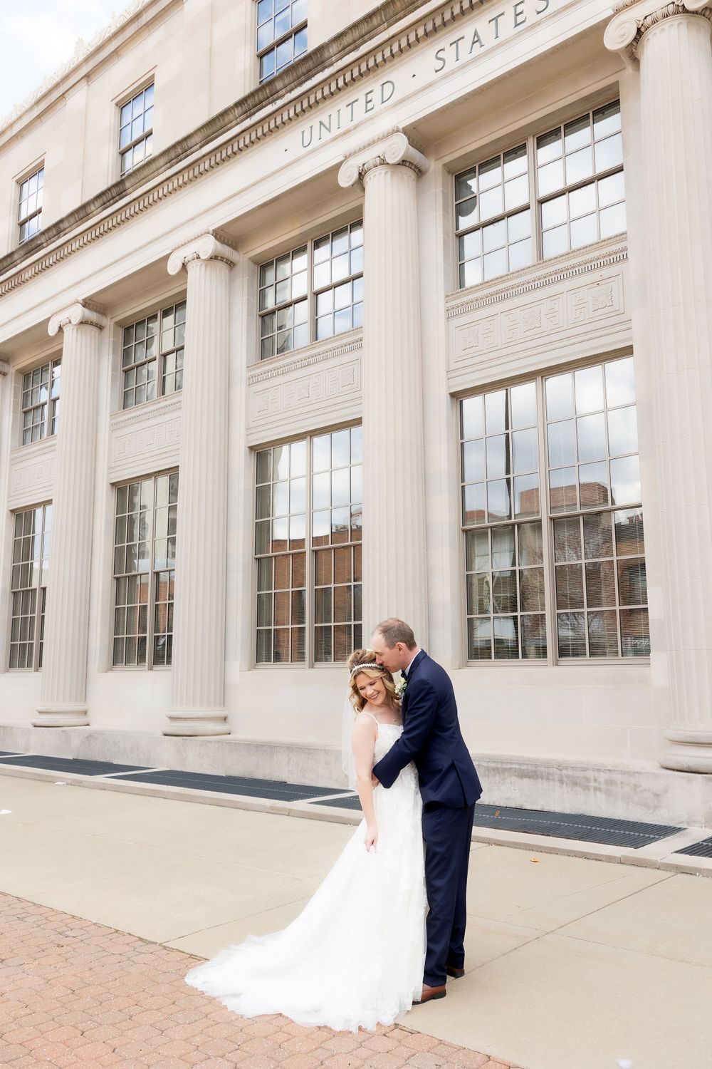 Bride and groom share intimate moment outside neoclassical building with columns.