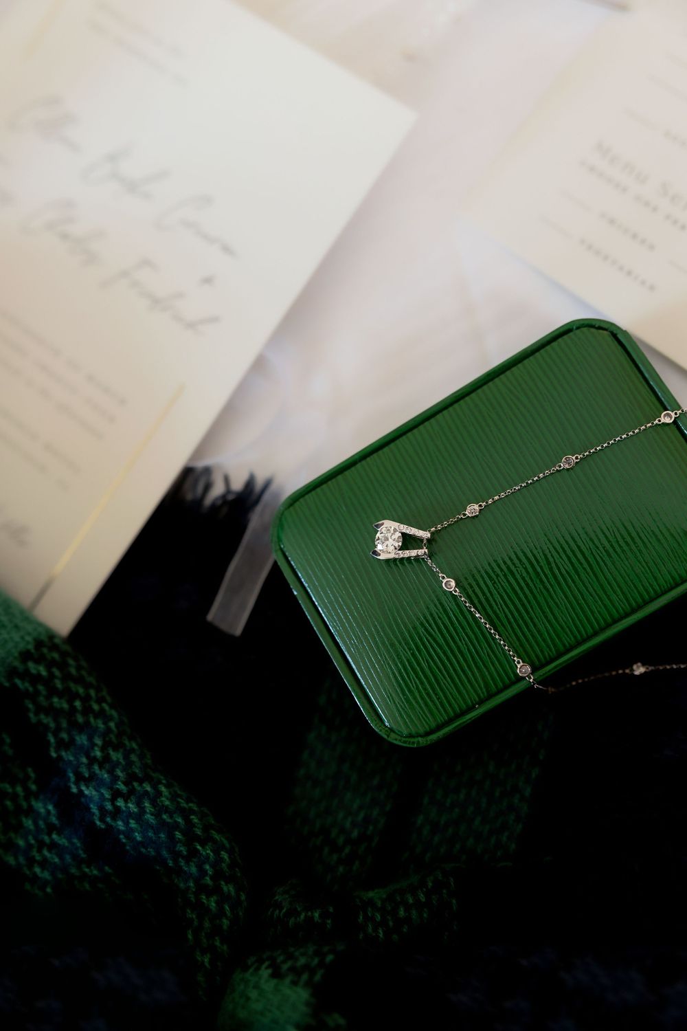 Green leather case with delicate necklace displayed on dark surface.