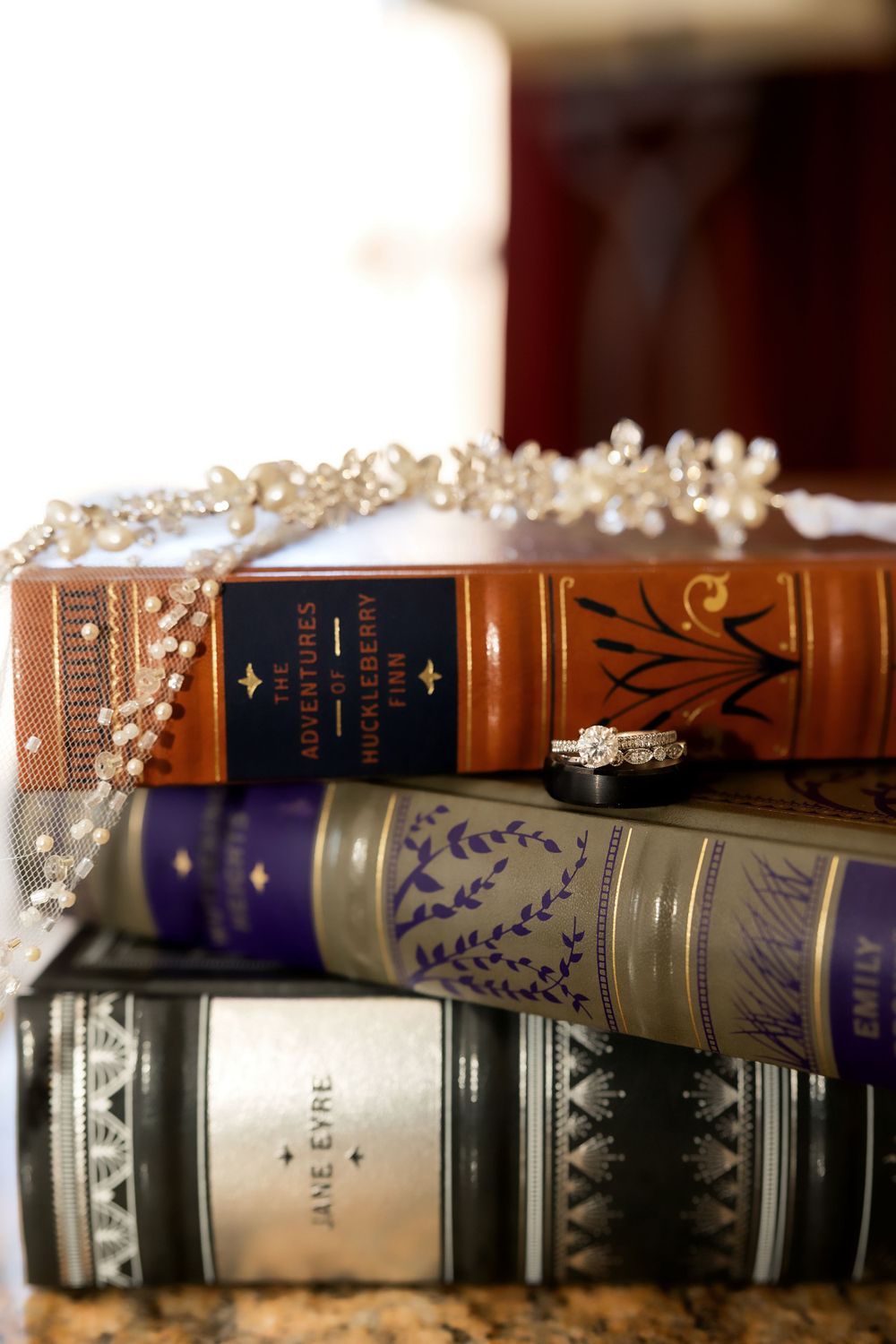 Stack of vintage books with pearl headpiece and engagement ring on top.