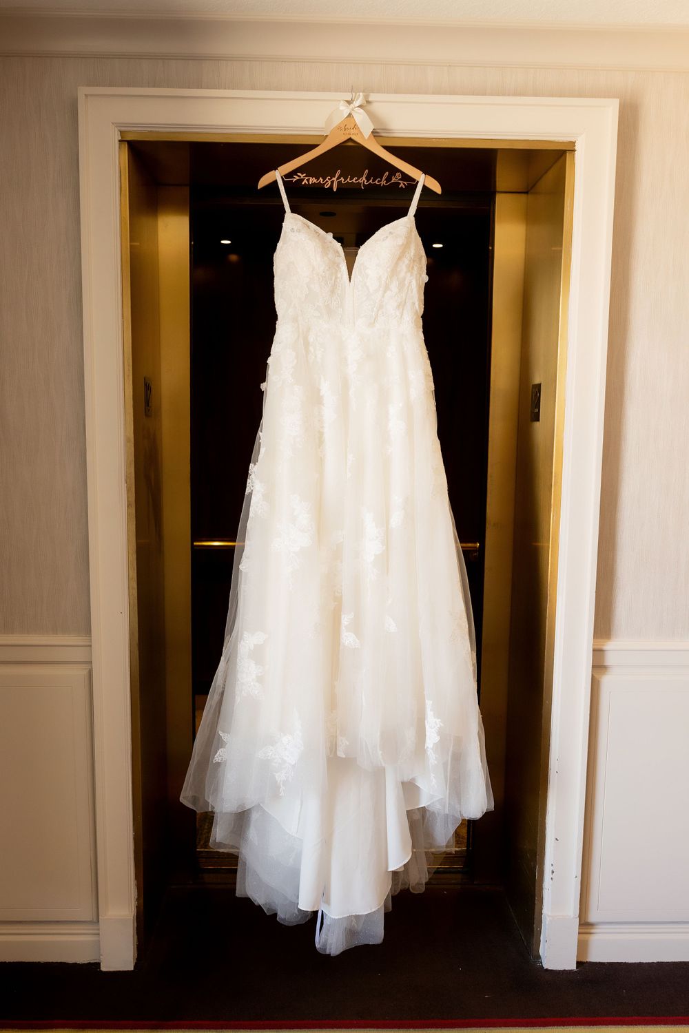 White lace wedding dress hanging in doorway on personalized hanger.