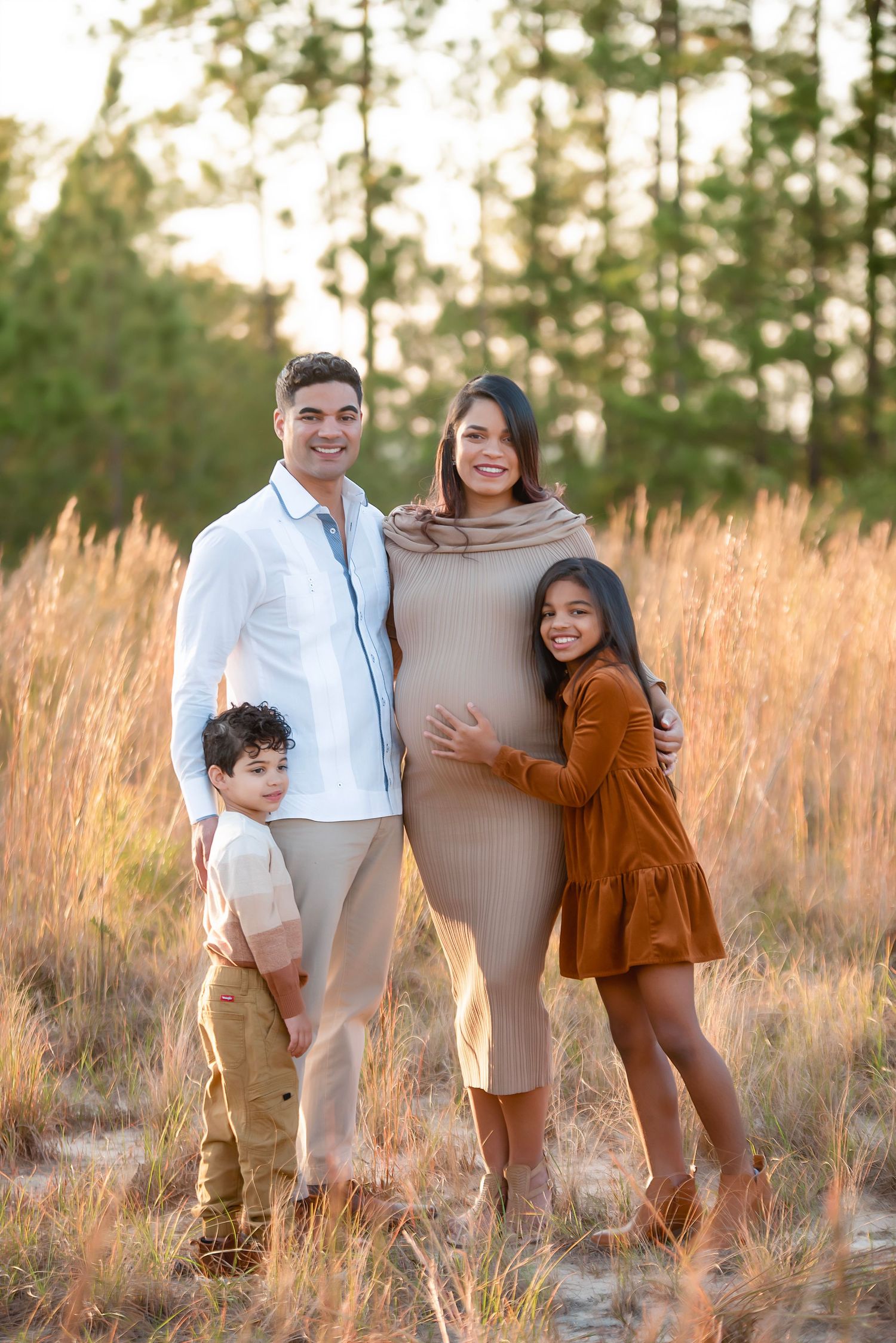 A family group portrait outdoors during autumn with natural fall foliage in the background.