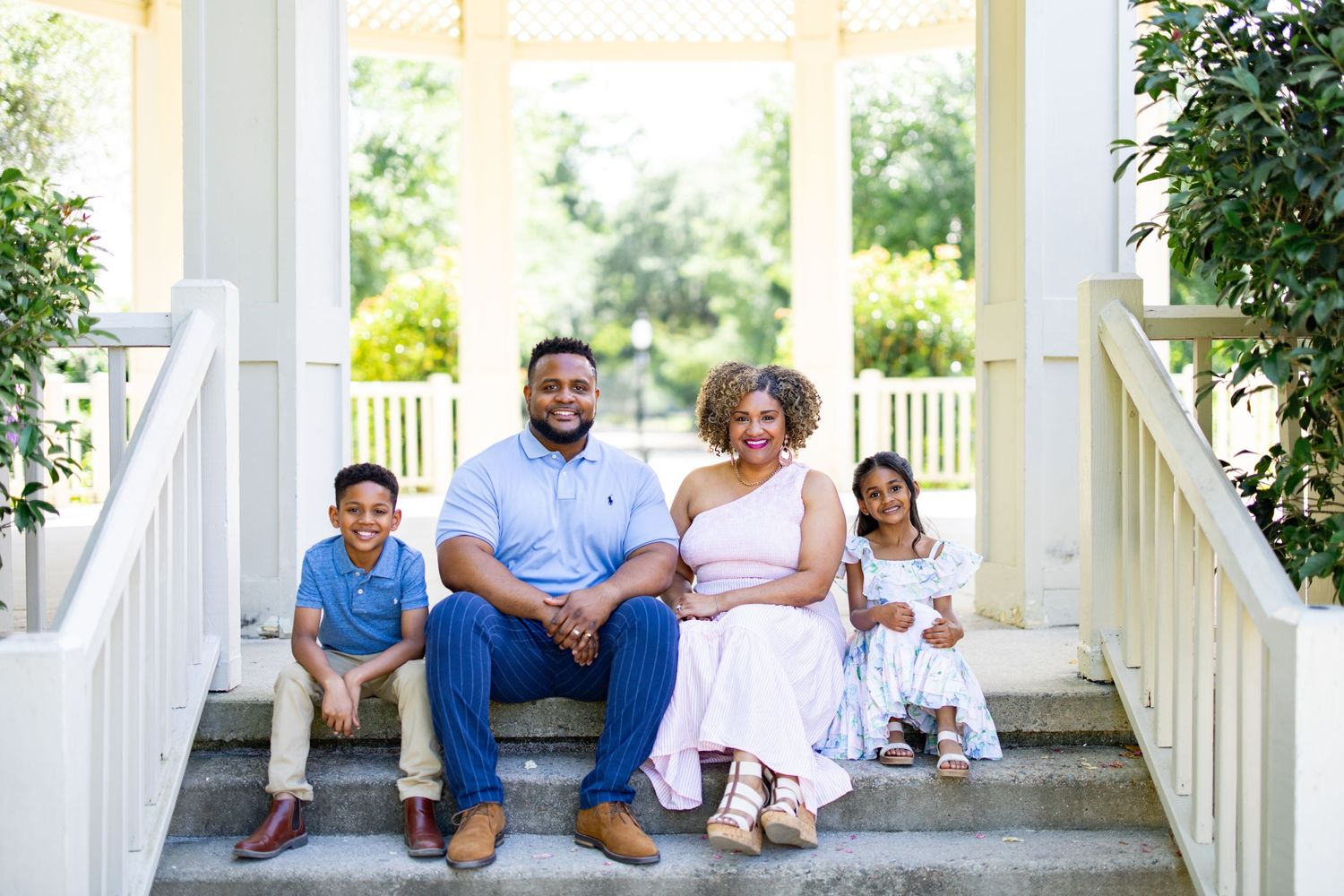 A family sits together on white porch steps during a sunny afternoon.